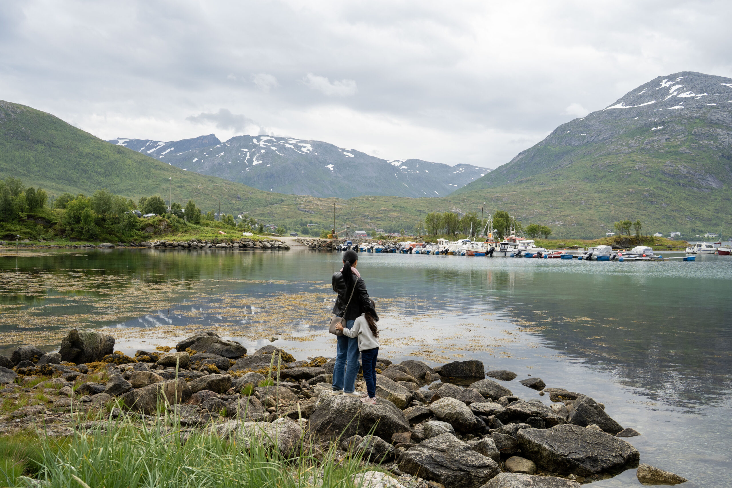 A mother with her daughter at the edge of the water of a fjord